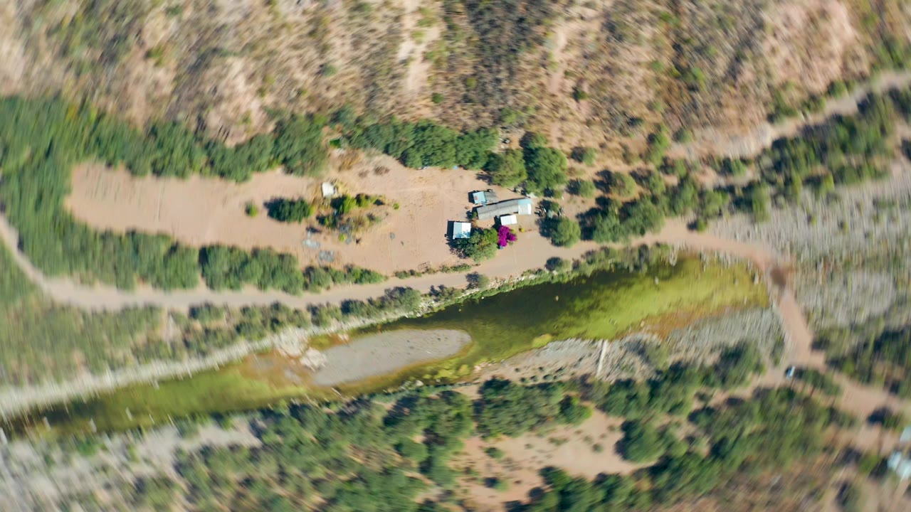 Blurred aerial frame of canal, dry terrain, trees, and dirt roads during drone movement.