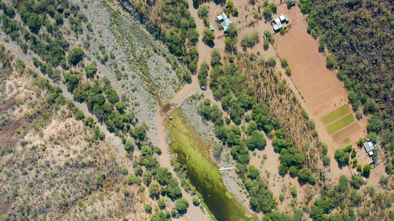 Aerial view of receding floodwater near muddy ground, trees, fields, and rural structures.