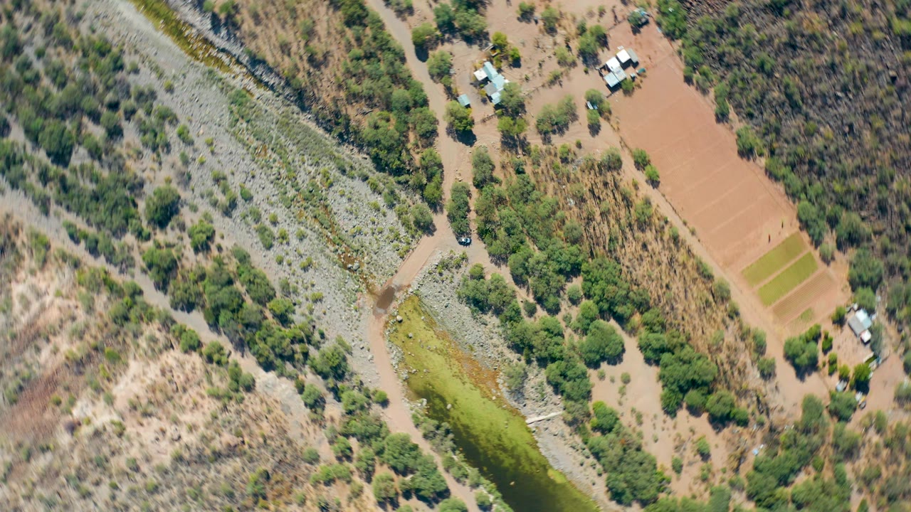 Aerial rural river bend with scrubland, road, buildings, and cultivated plots.