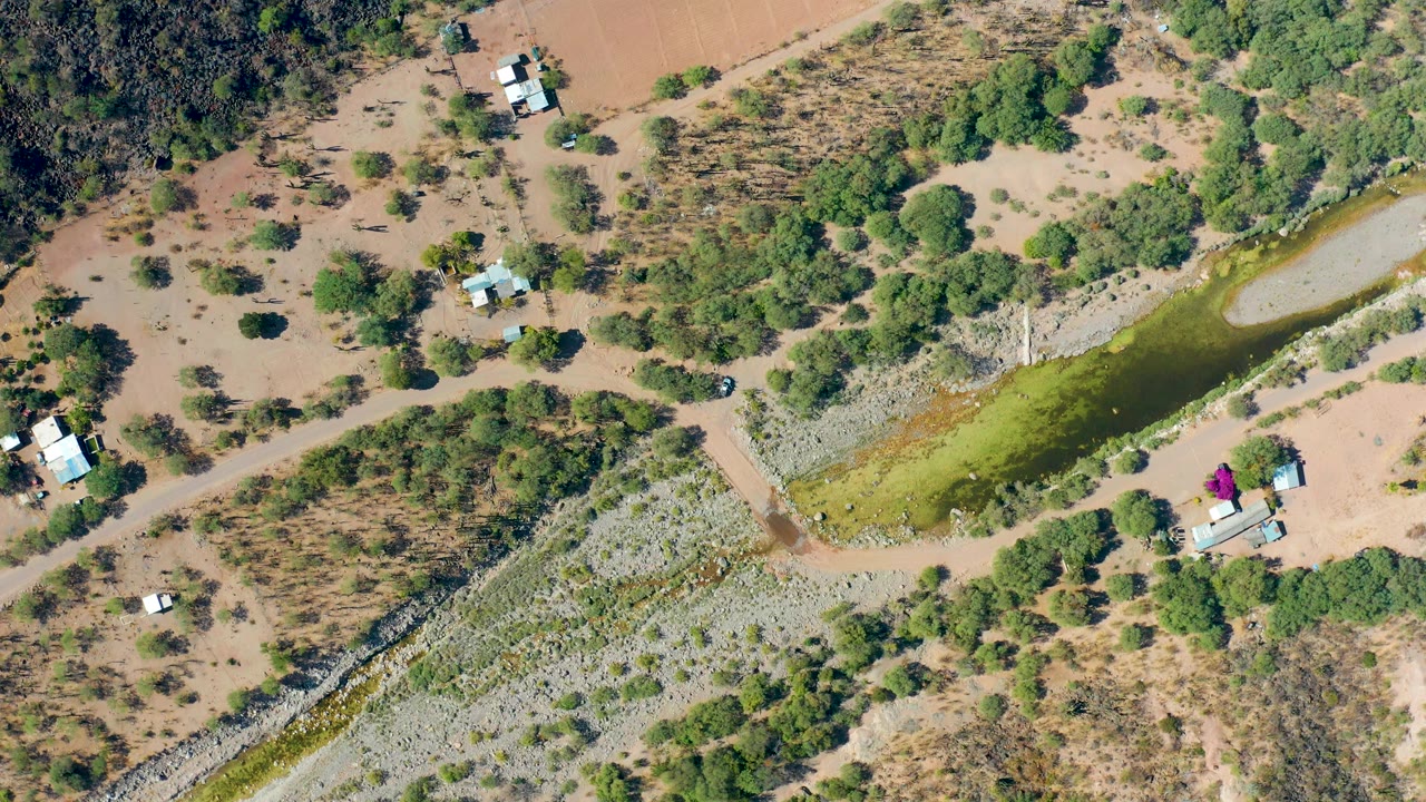 Aerial canal view with dry ground, trees, and small buildings nearby.