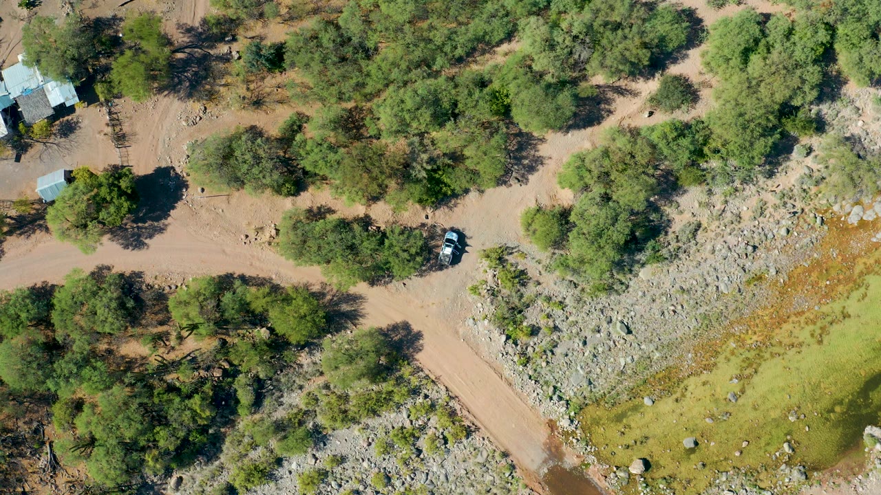 Drone view of a dirt road bordered by trees and rocky open land.