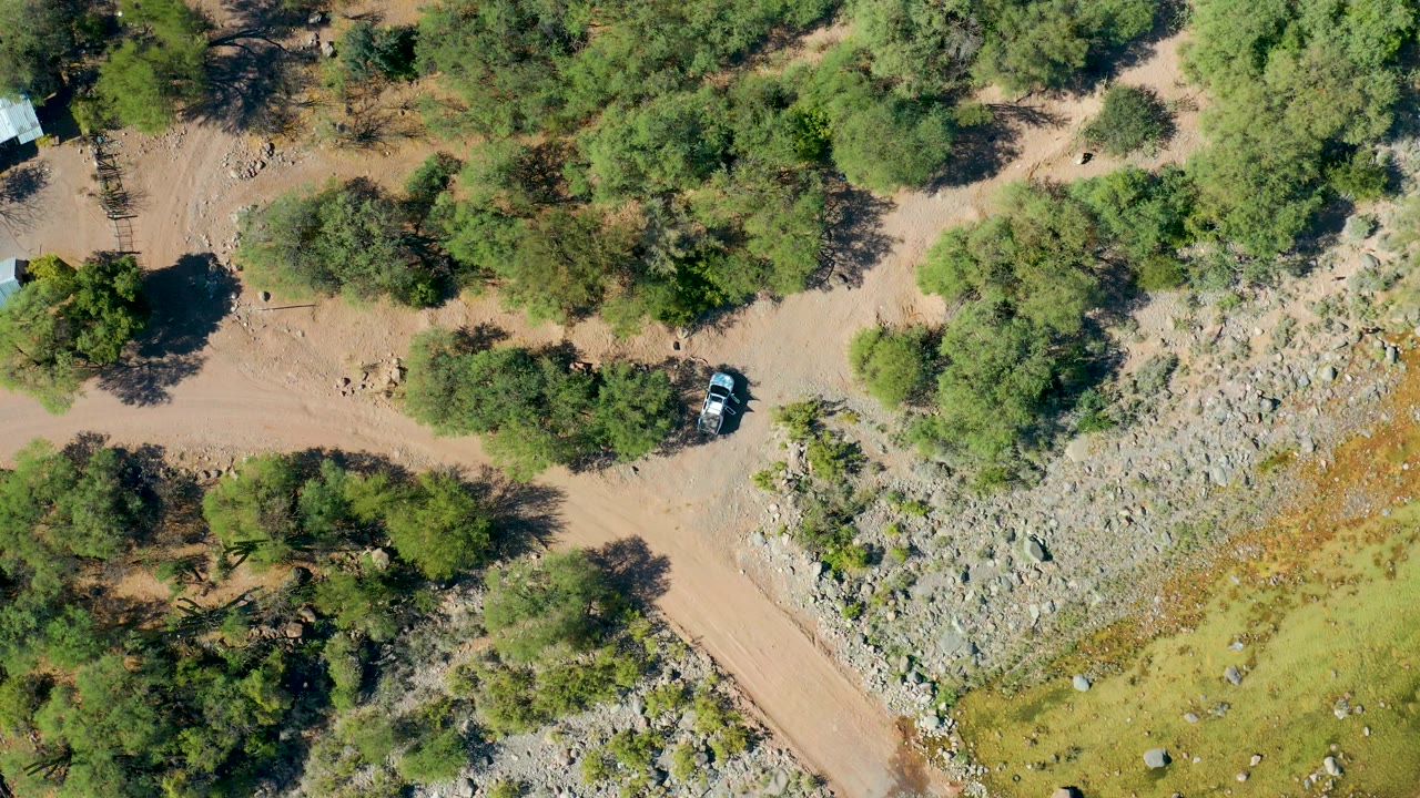 Drone view of a car on a rural dirt track beside a rocky slope.