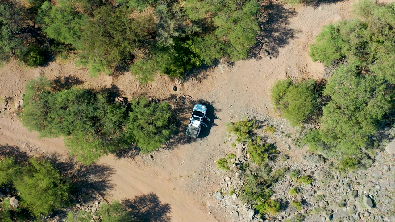 Overhead view of a car on a sandy dirt trail among green trees.