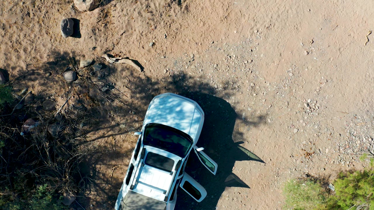 White car seen from above beside rocks and brush on a dirt road