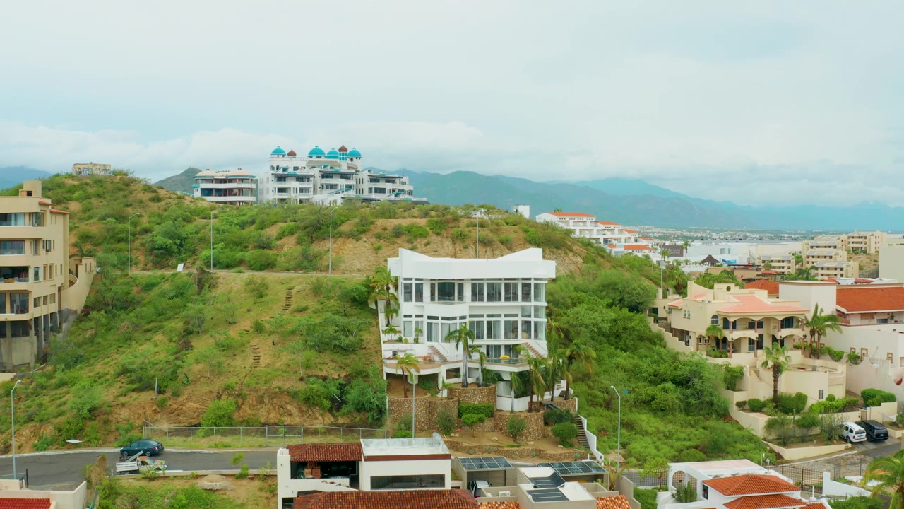 Residential hillside with white buildings, road, and distant mountains.