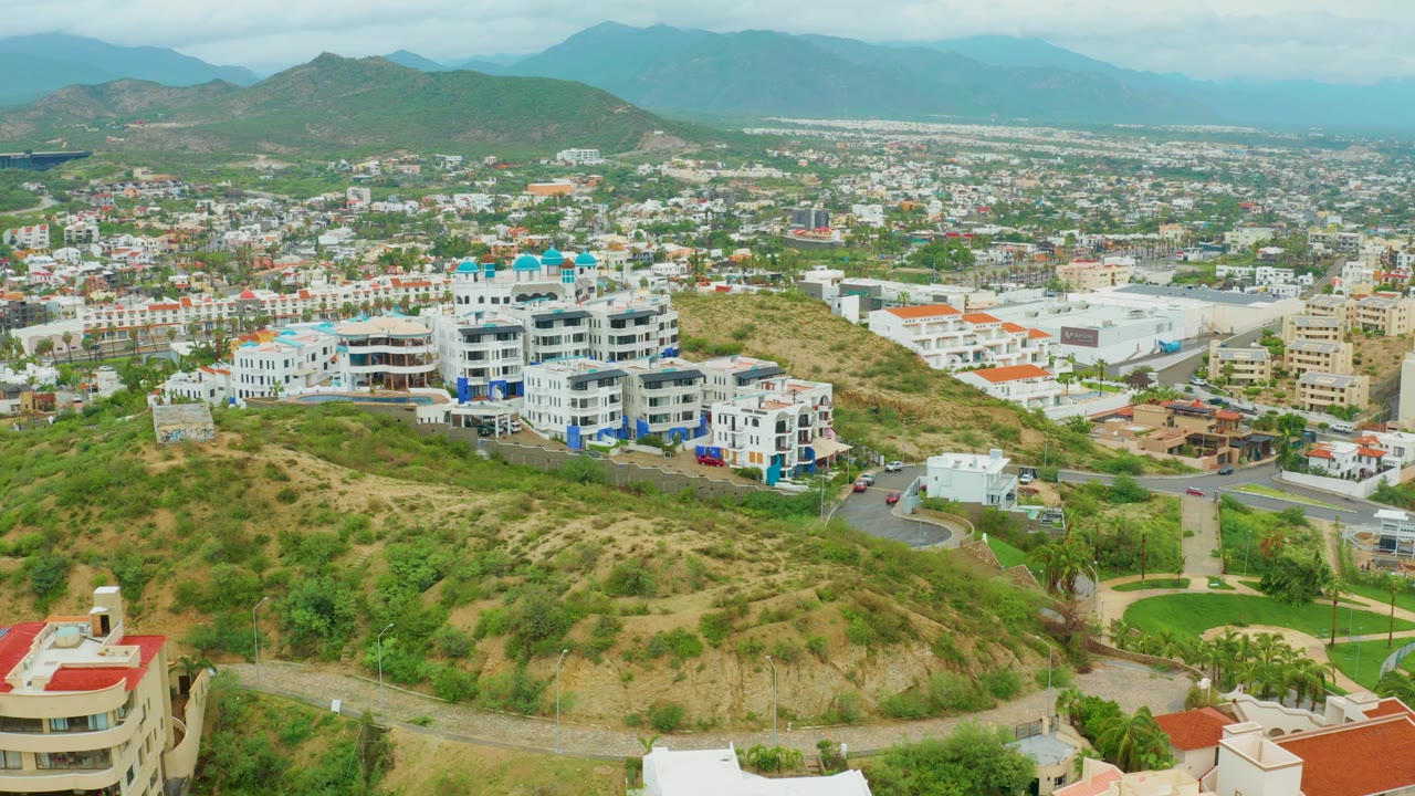 Aerial neighborhood view with white buildings, curving road, and mountain backdrop.