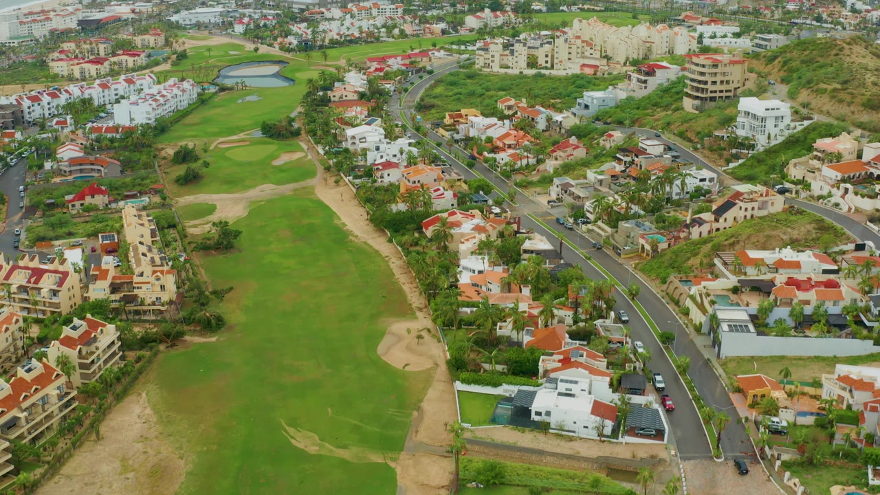Golf course, road traffic, homes, and distant water viewed from above.