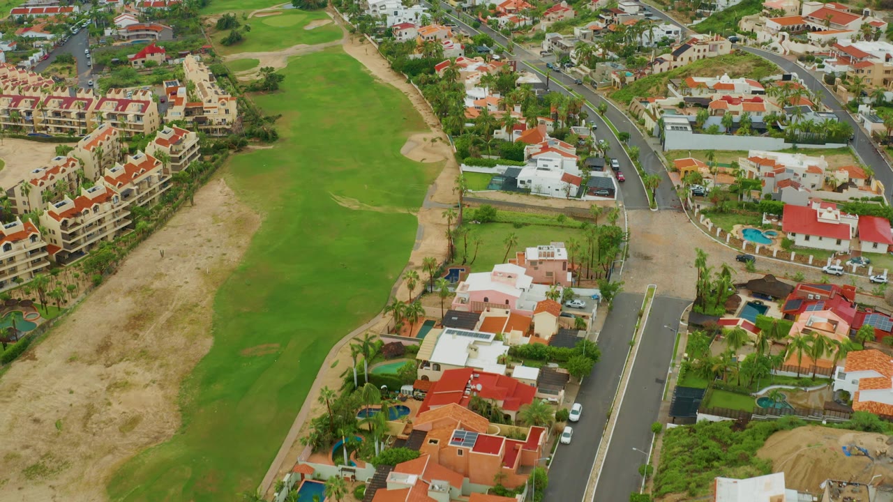 Residential golf course aerial with homes, road, fairway, and hillside buildings.