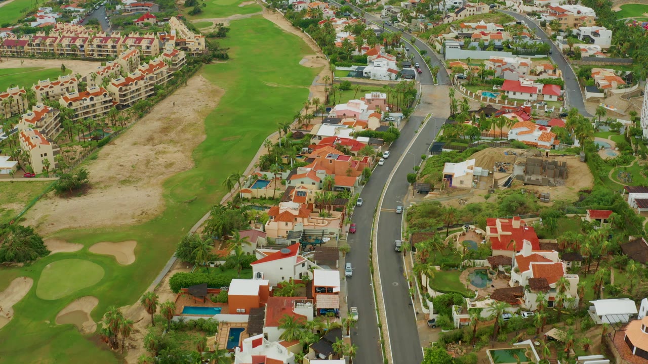 Drone view over homes, fairways, sand traps, and a road with cars.