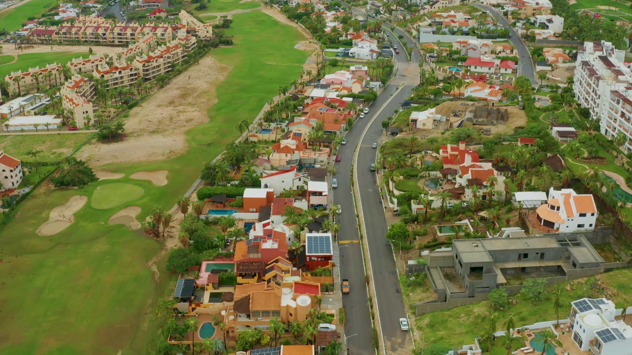 Aerial neighborhood view with golf greens, homes, and a central road.