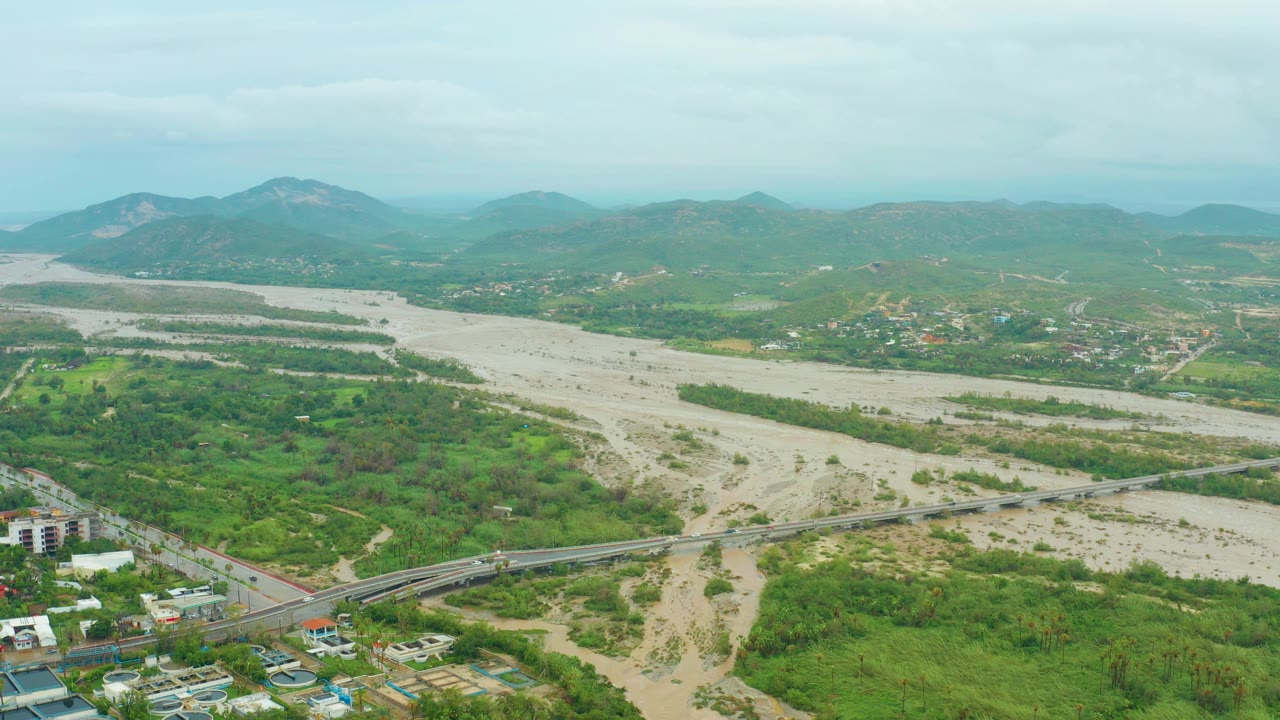 Aerial valley landscape with bridge crossing a broad muddy river.