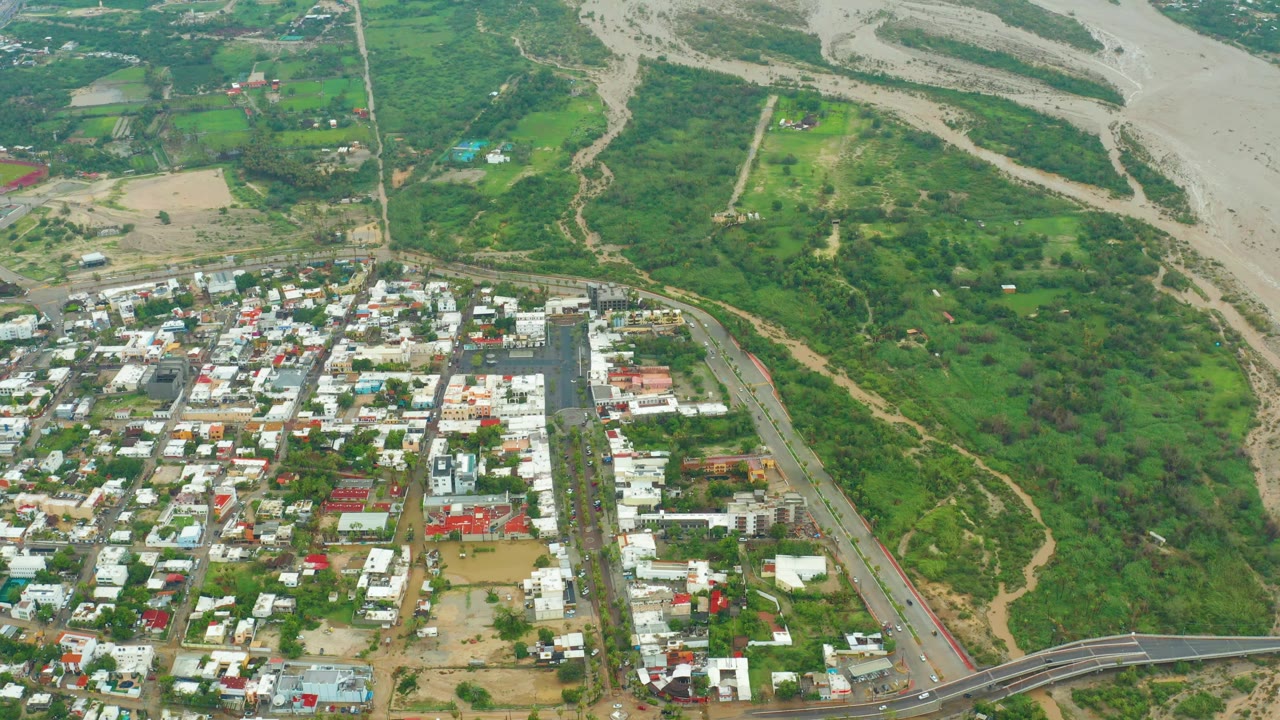 Aerial view of receding floodwater near roads, homes, and green riverbank land.