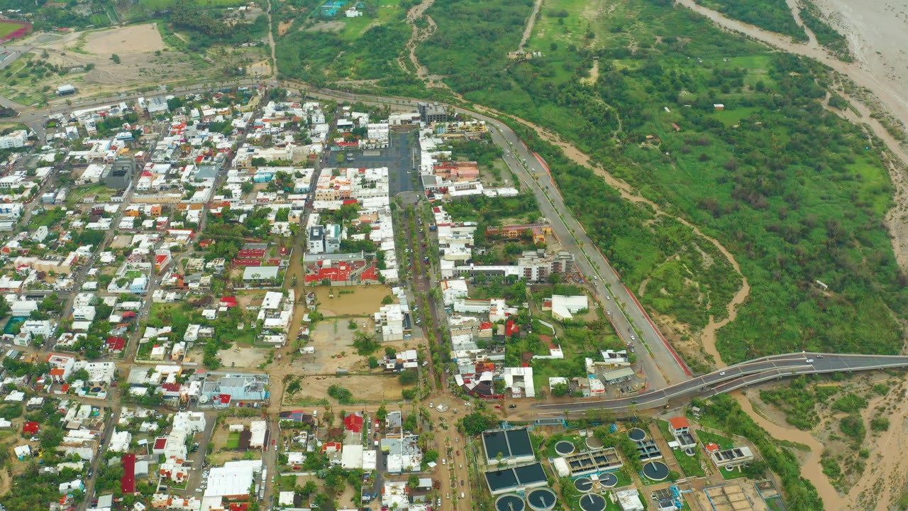 Aerial frame of a town edge with homes, roads, and green land.