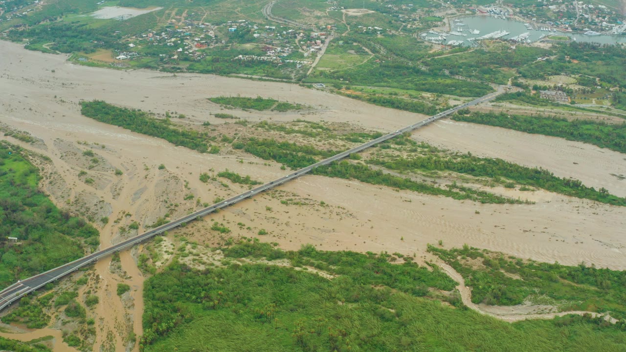 High aerial view of muddy water flowing under a long bridge.
