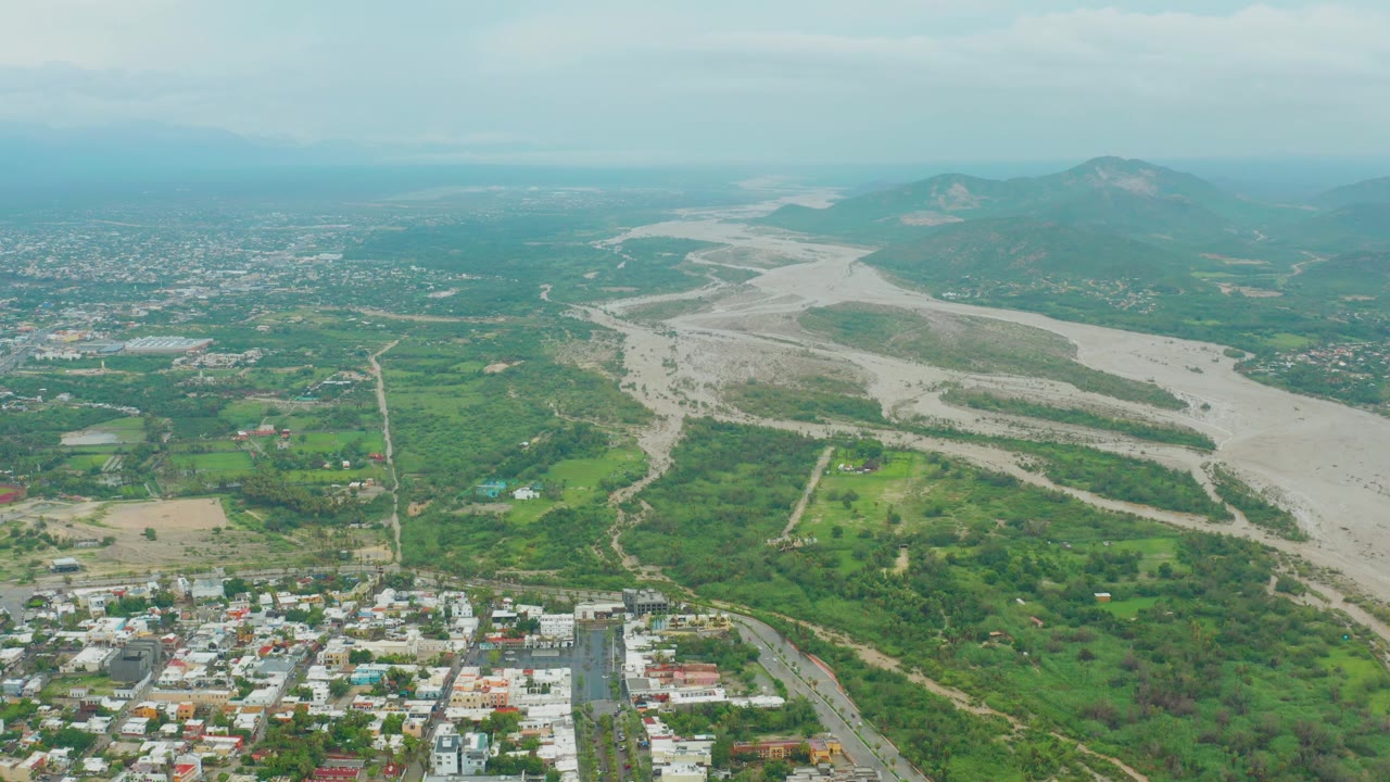 Aerial landscape with a winding riverbed, green fields, and low buildings.