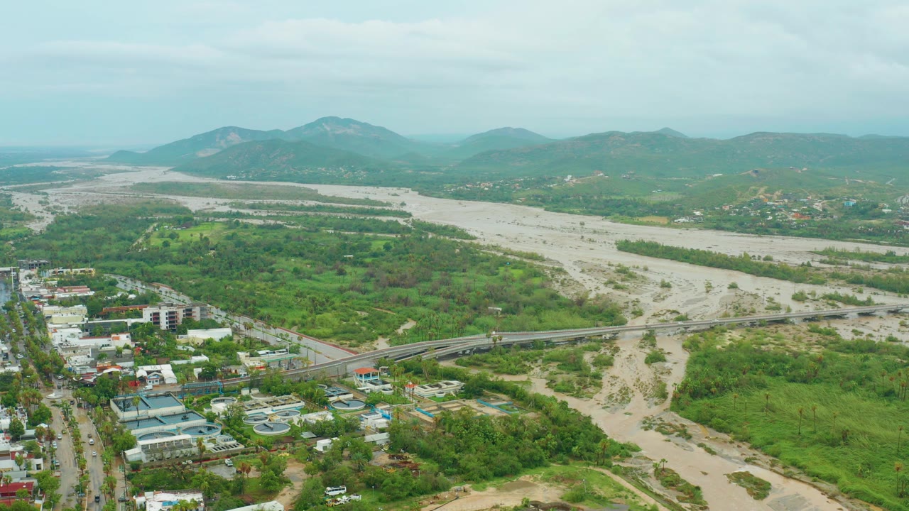 Third frame shows the San Jose del Cabo BCS Mexico river landscape from above, with pale sediment bars, shallow muddy flow, the bridge at the lower midframe, roadside buildings, thick green vegetation, mountains, and no visible people.