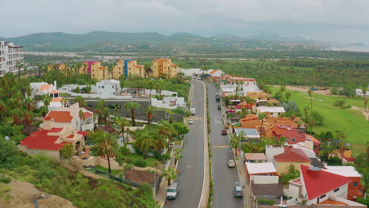 Curving residential road with homes, palms, and mountains in the distance.