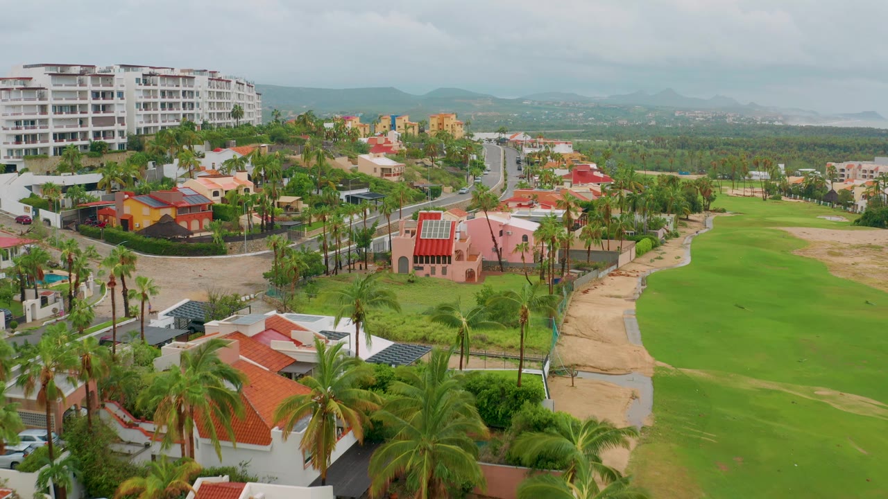 Aerial frame with resort road, homes, palms, and golf course fairway.