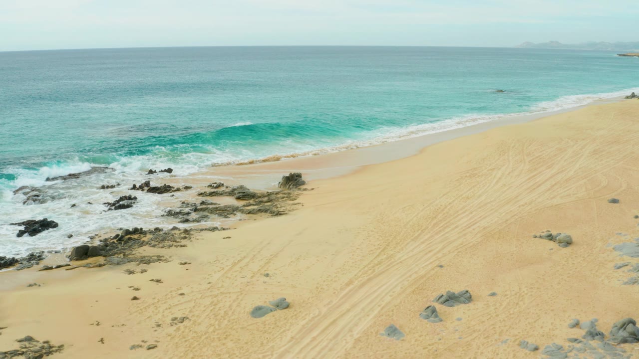Waves breaking around dark rocks beside a broad sandy beach