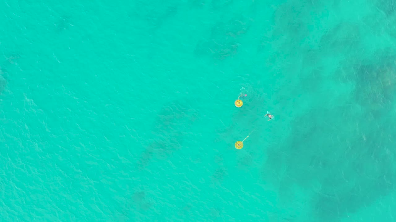 Clear turquoise water in Laguna Beach Los Cabos shows two yellow buoys and a tiny swimmer positioned just to the right of the markers.