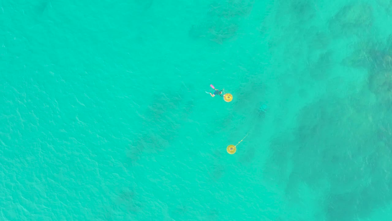 Small swimmers and yellow floats in clear turquoise water.