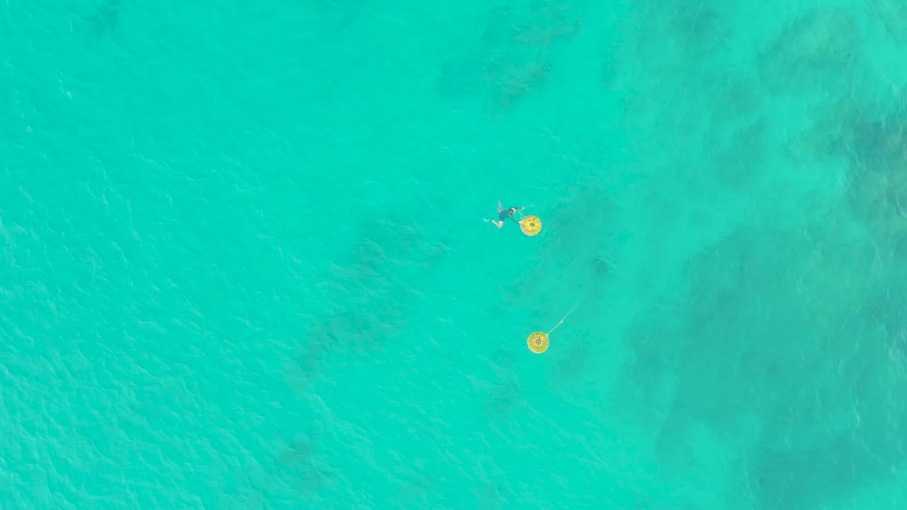 At Laguna Beach Los Cabos, the overhead frame keeps the swimmers and yellow floats near the upper left area against a broad turquoise water background.