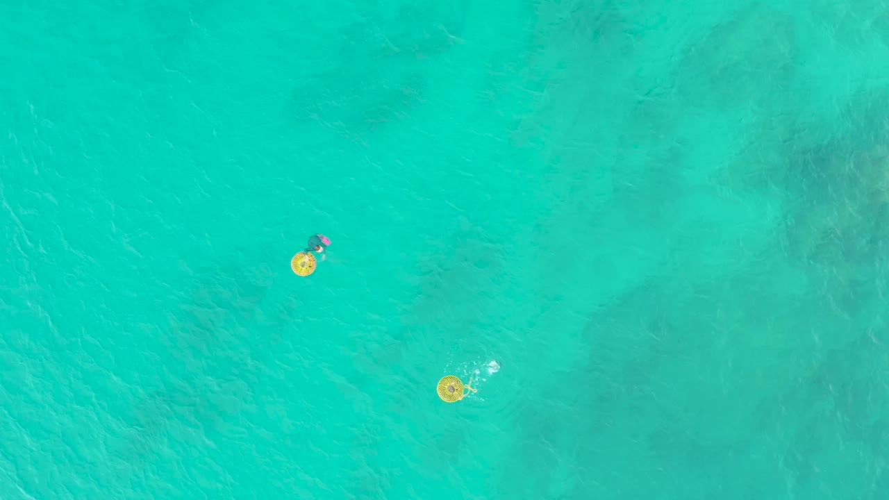 At 0:02 in Laguna Beach Los Cabos, the upper person and lower person drift slightly while their yellow rings stand out against pale turquoise water.
