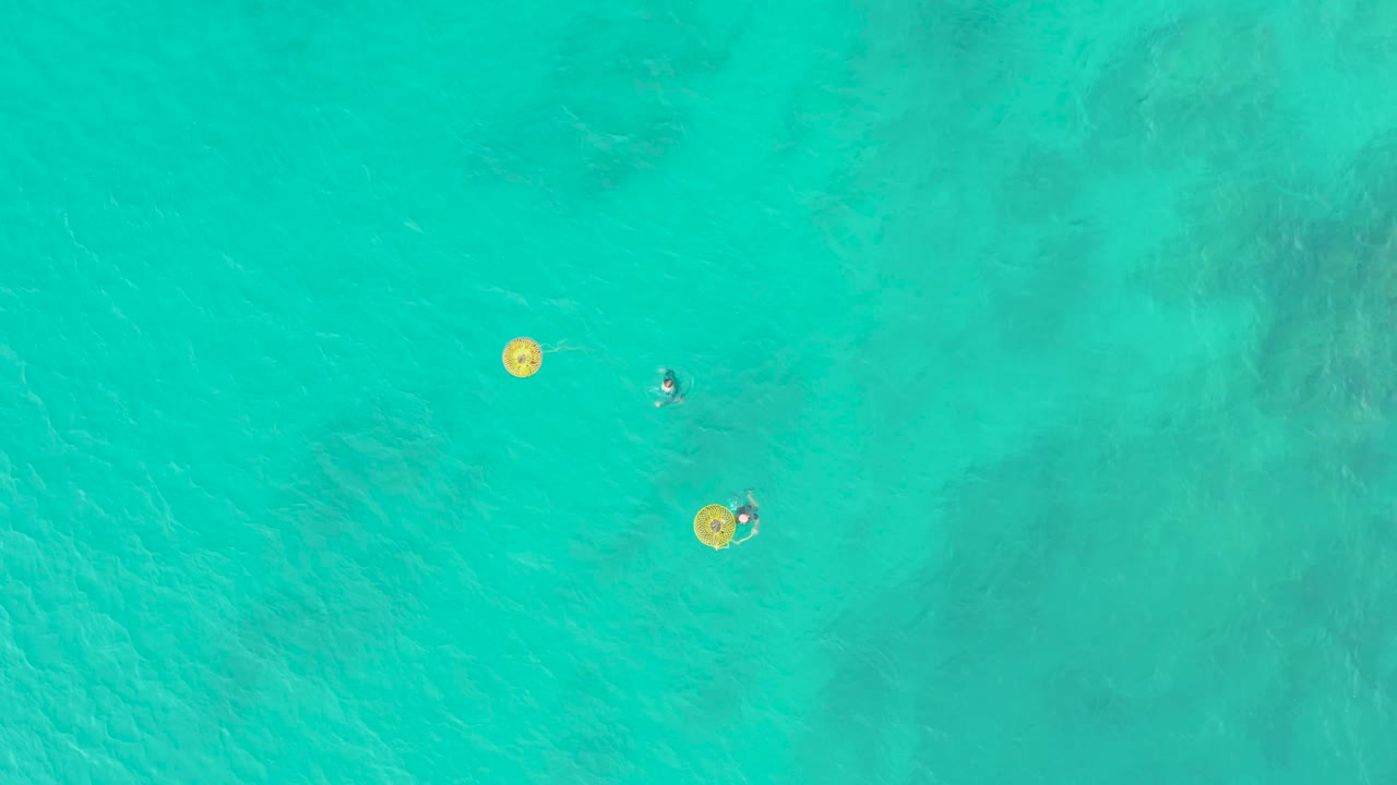 Swimmers and yellow float rings separated in clear water.