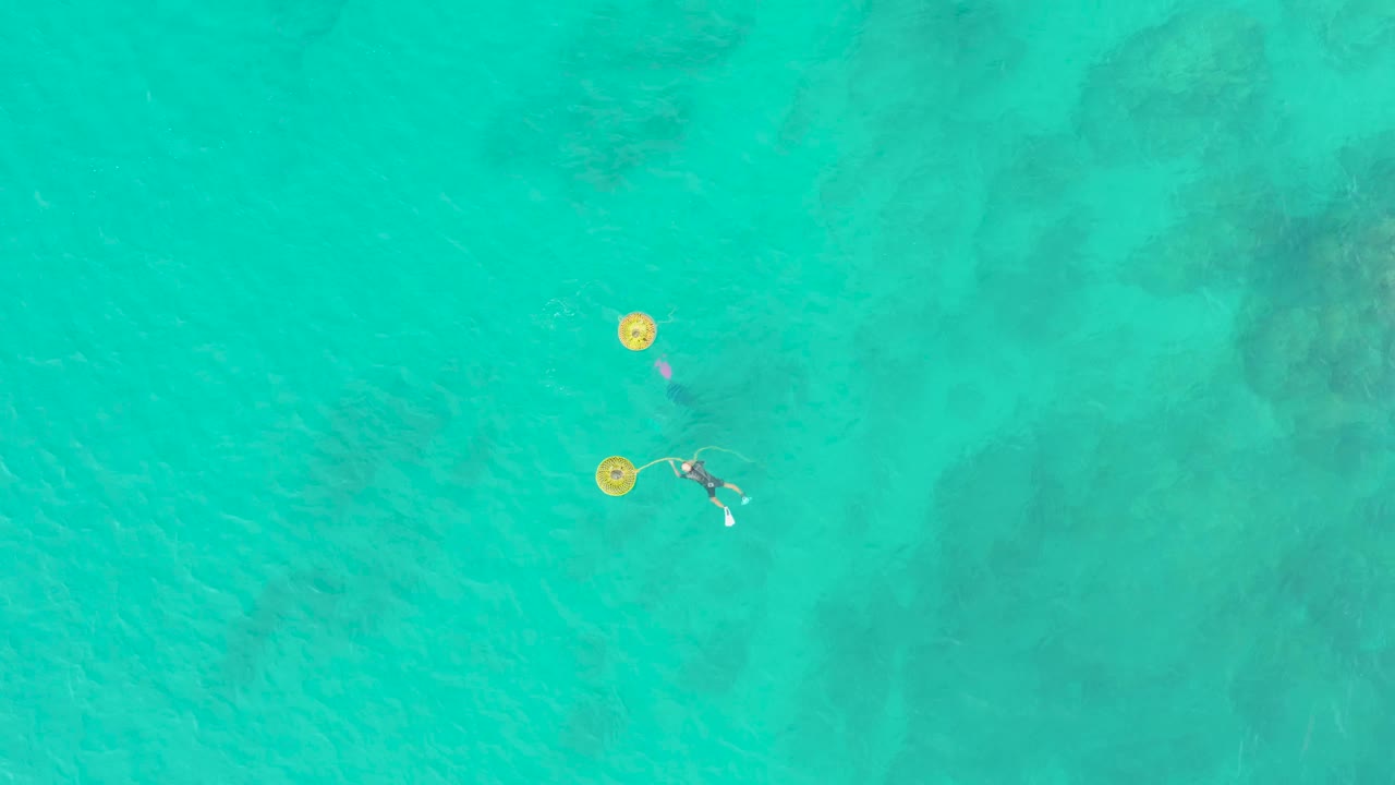 Two swimmers near yellow circular floats in clear ocean water.