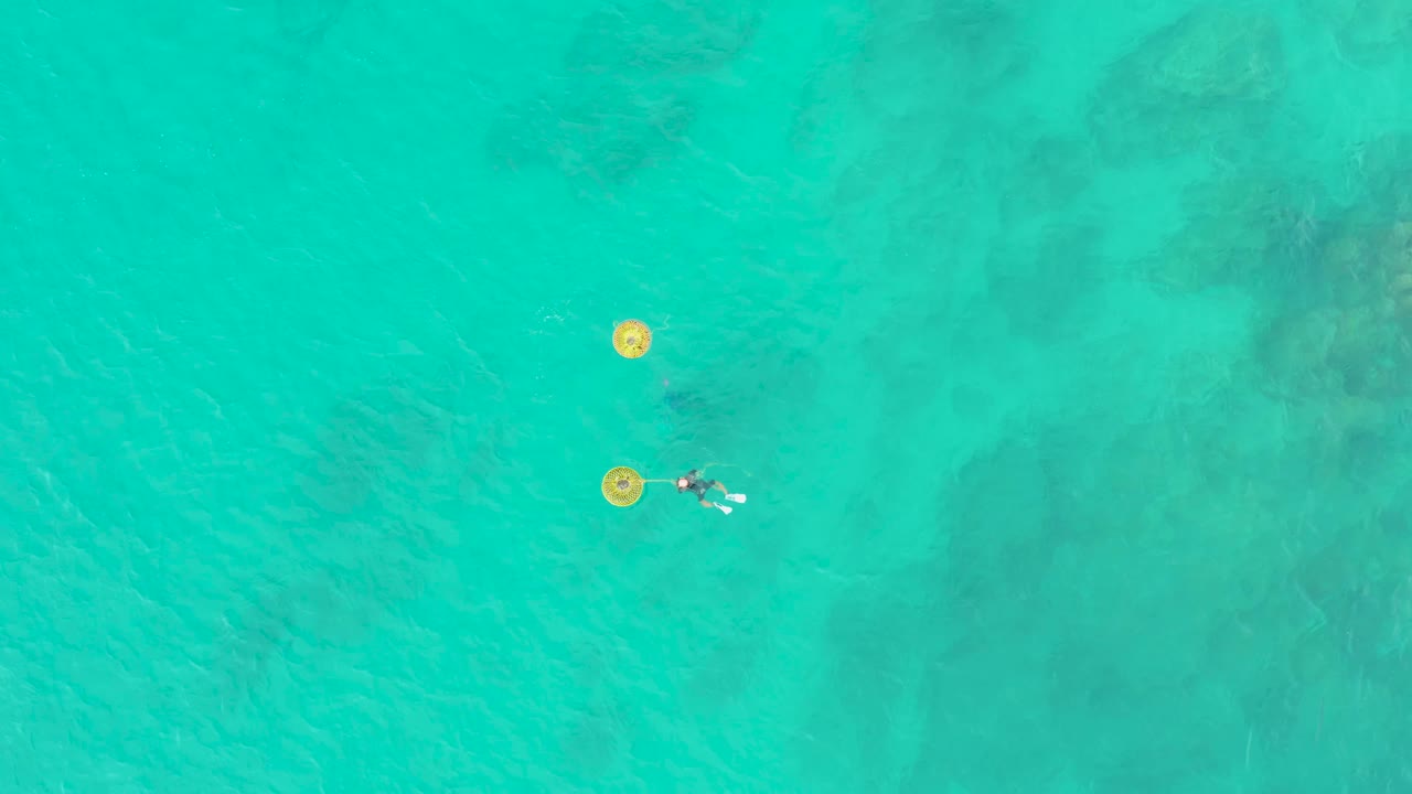 At 0:02, the overhead frame keeps the two swimmers near the left side while yellow buoys sit above them in bright turquoise water at Laguna Beach Los Cabos.