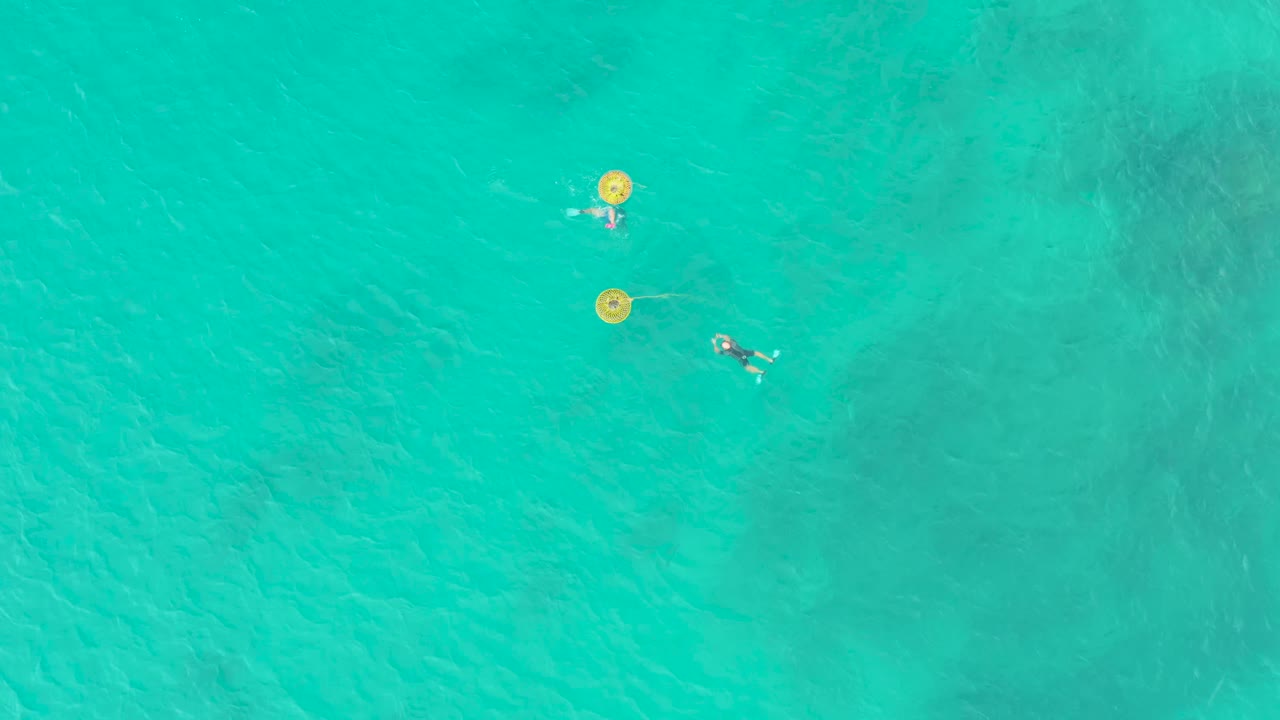 Laguna Beach Los Cabos aerial view with two yellow buoys aligned on the left side of the swimmers, while the lower swimmer moves across the clear water.