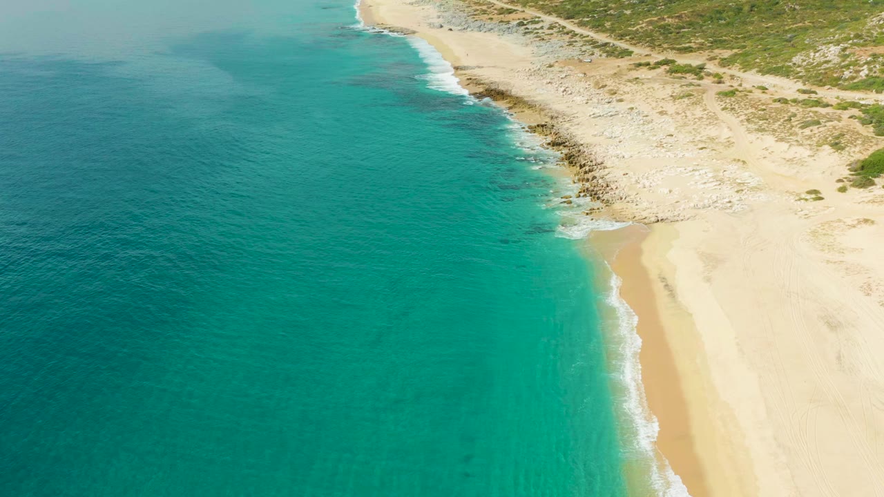 Aerial view in Laguna Beach Los Cabos with the shoreline running diagonally, bright turquoise sea filling most of the frame, pale sand at right, and no visible people.