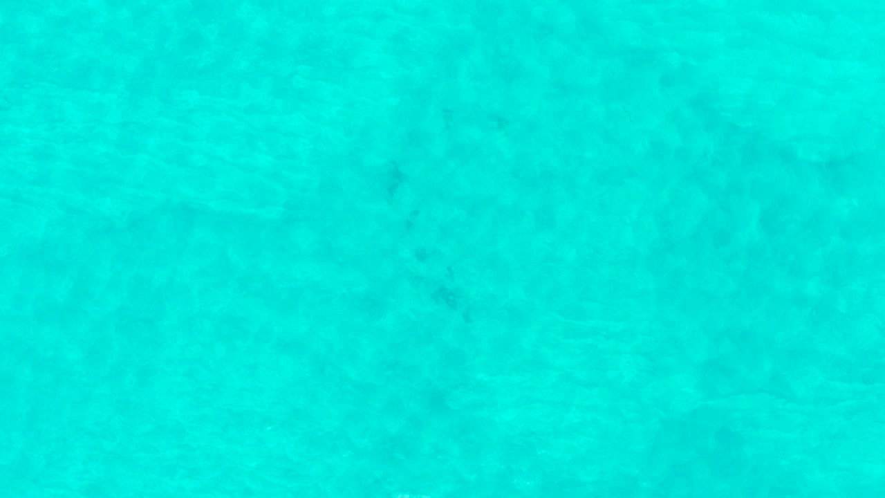 Bright turquoise ocean water at Laguna Beach Los Cabos shows soft darker patches below the surface, light surface movement, and no visible people.