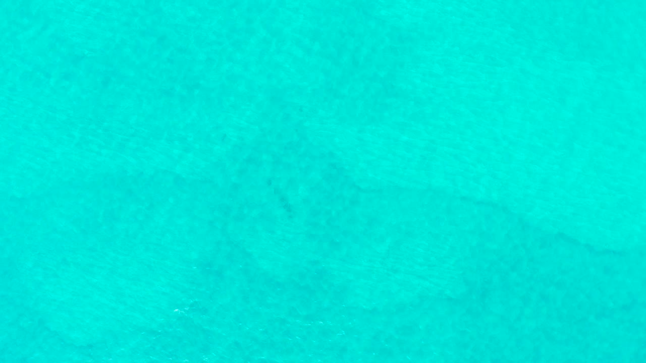 Turquoise shallow ocean water at Laguna Beach Los Cabos fills the opening frame, with faint darker seabed features under the surface and no visible people.