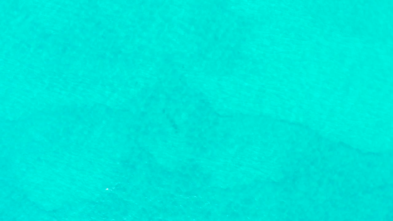 Clear blue-green ocean water in Laguna Beach Los Cabos shows soft ripples shifting across the surface, with muted seabed shapes visible below and no visible people.