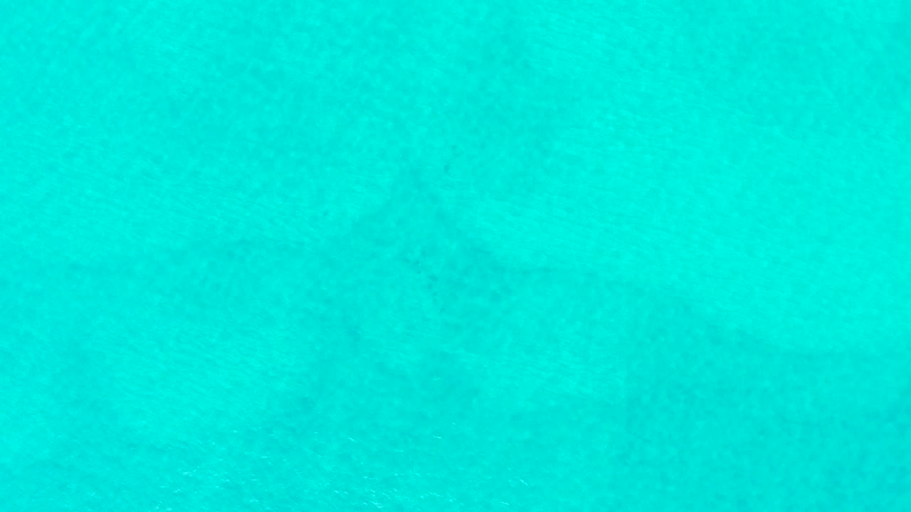 Overhead view of turquoise water at Laguna Beach Los Cabos with a faint dark shark form beneath the surface and no visible people.