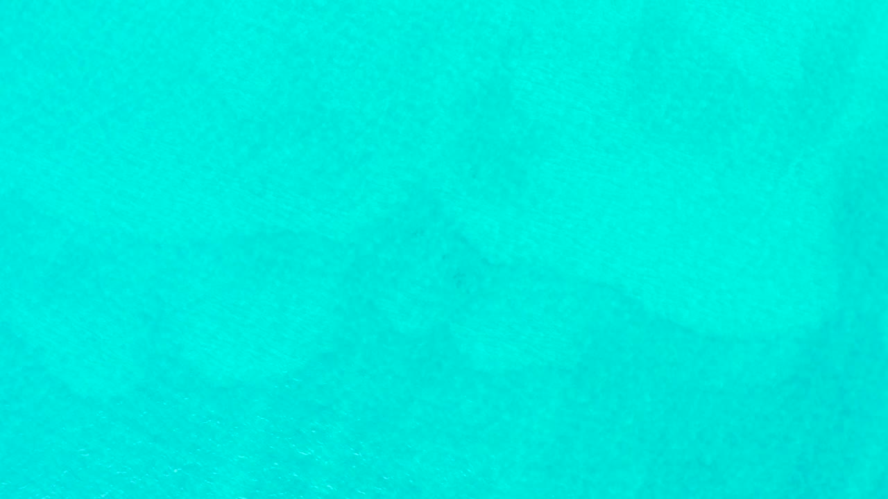 At 0:02, the overhead view shows turquoise ocean surface and a muted dark shark silhouette moving through the water, with no visible people.