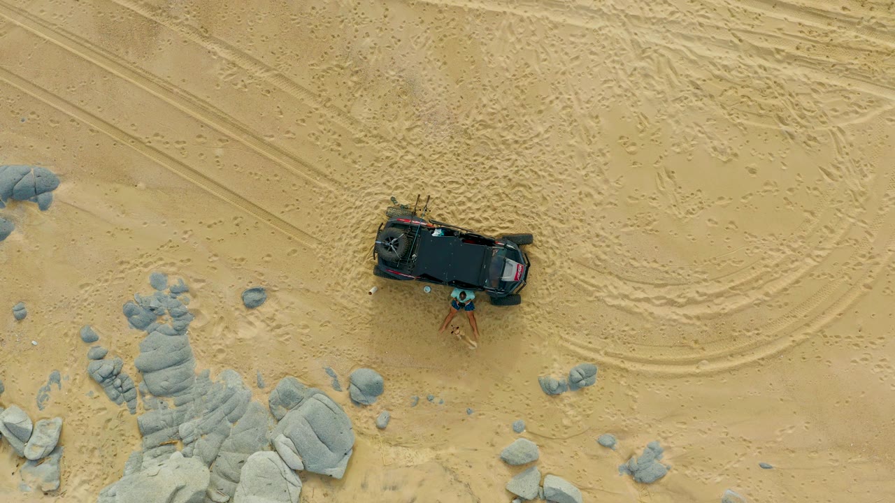 Black SUV parked on sand with rock clusters along the left edge and tracks across the ground.