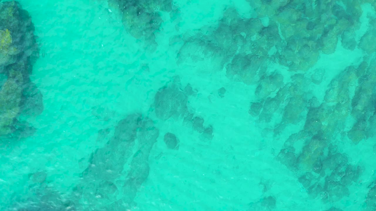 Overhead view of turquoise water at Laguna Beach Los Cabos with dark submerged rocks near the upper and left edges and no visible people.
