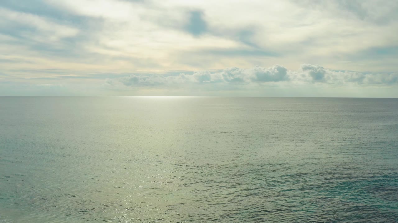 At Laguna Beach Los Cabos, calm ocean water stretches to a cloudy horizon with a pale band of sunlight on the surface and no visible people.