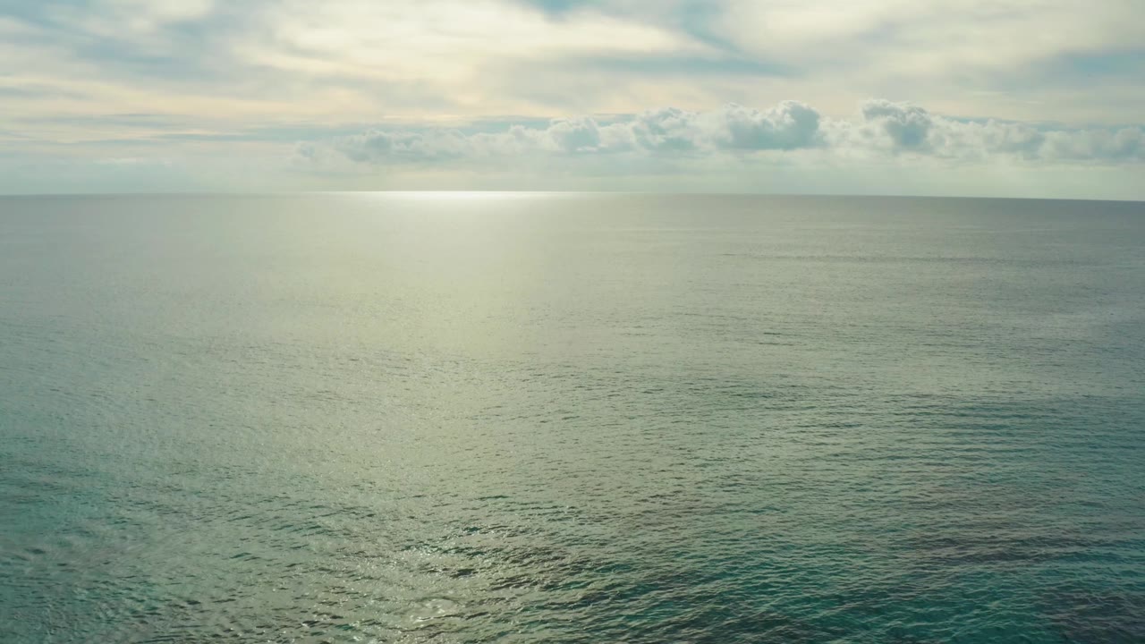 Wide ocean view with soft sun reflection beneath a muted cloud layer.