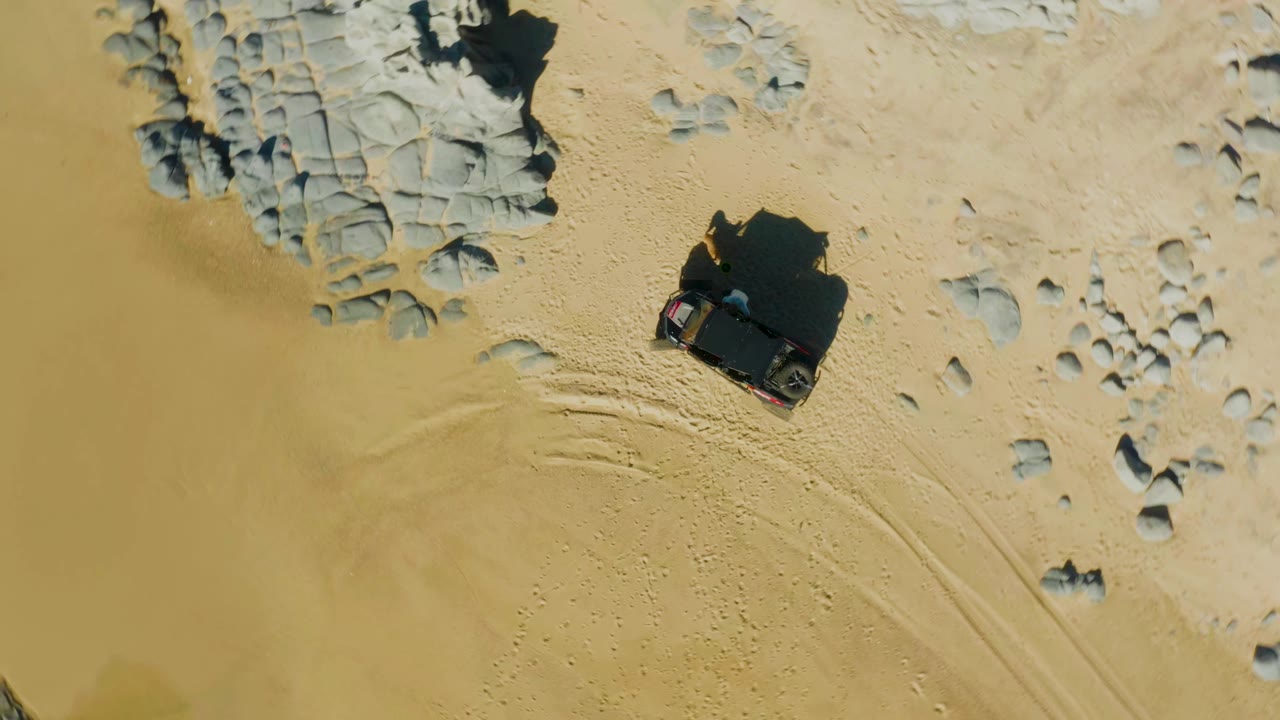 SUV moving across sand near scattered rocks and tire tracks