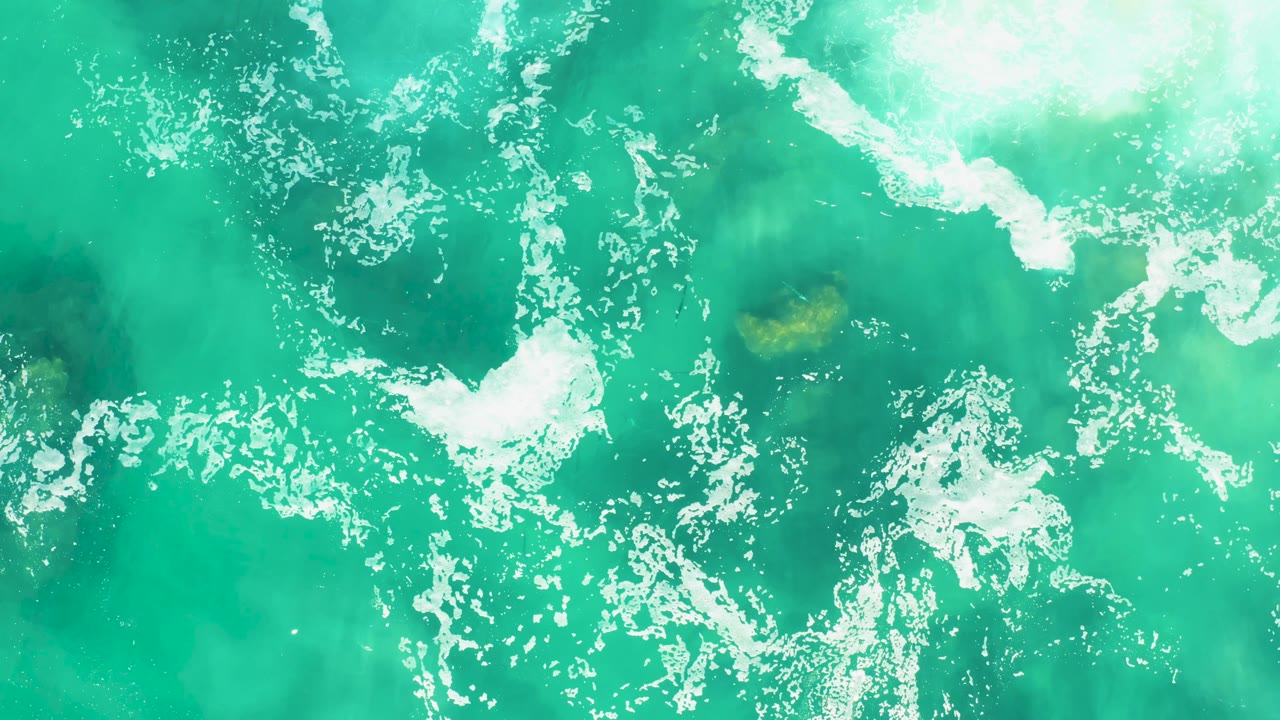 Overhead ocean water with a curved band of white foam.