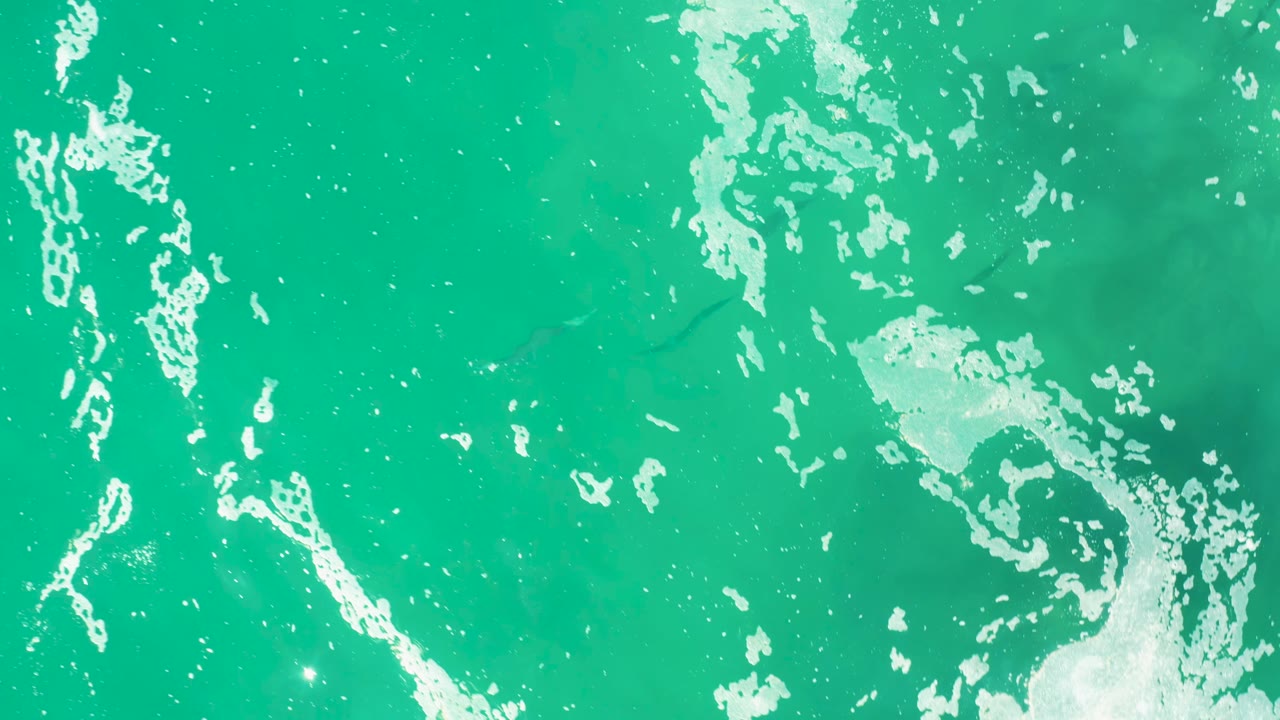 Top-down view of turquoise ocean water and scattered white seafoam in Laguna Beach Los Cabos, Baja California Sur, with no visible people.
