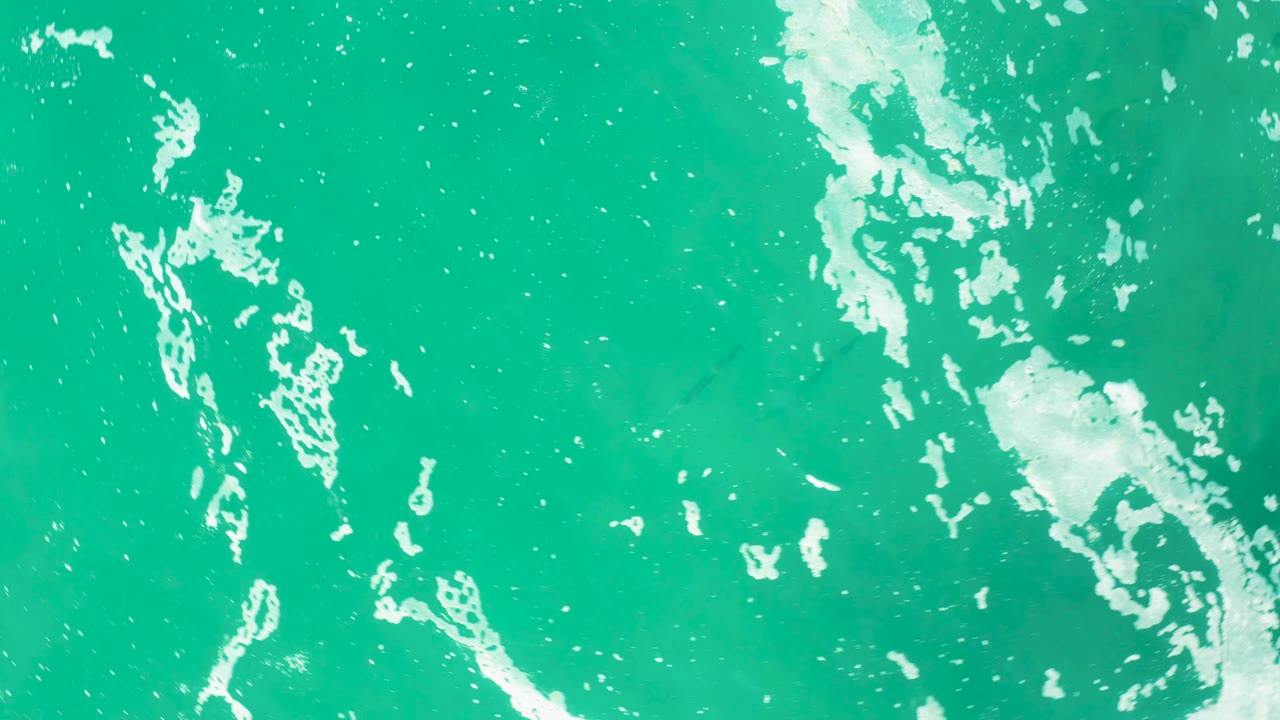 Top-down ocean surface in Laguna Beach Los Cabos with broken white foam patterns crossing turquoise water and no visible people or vessels.