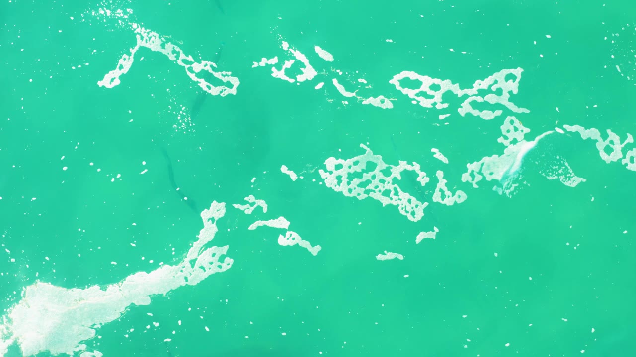Curving white foam patches cross the turquoise sea surface at Laguna Beach Los Cabos, with no visible people or vessels.