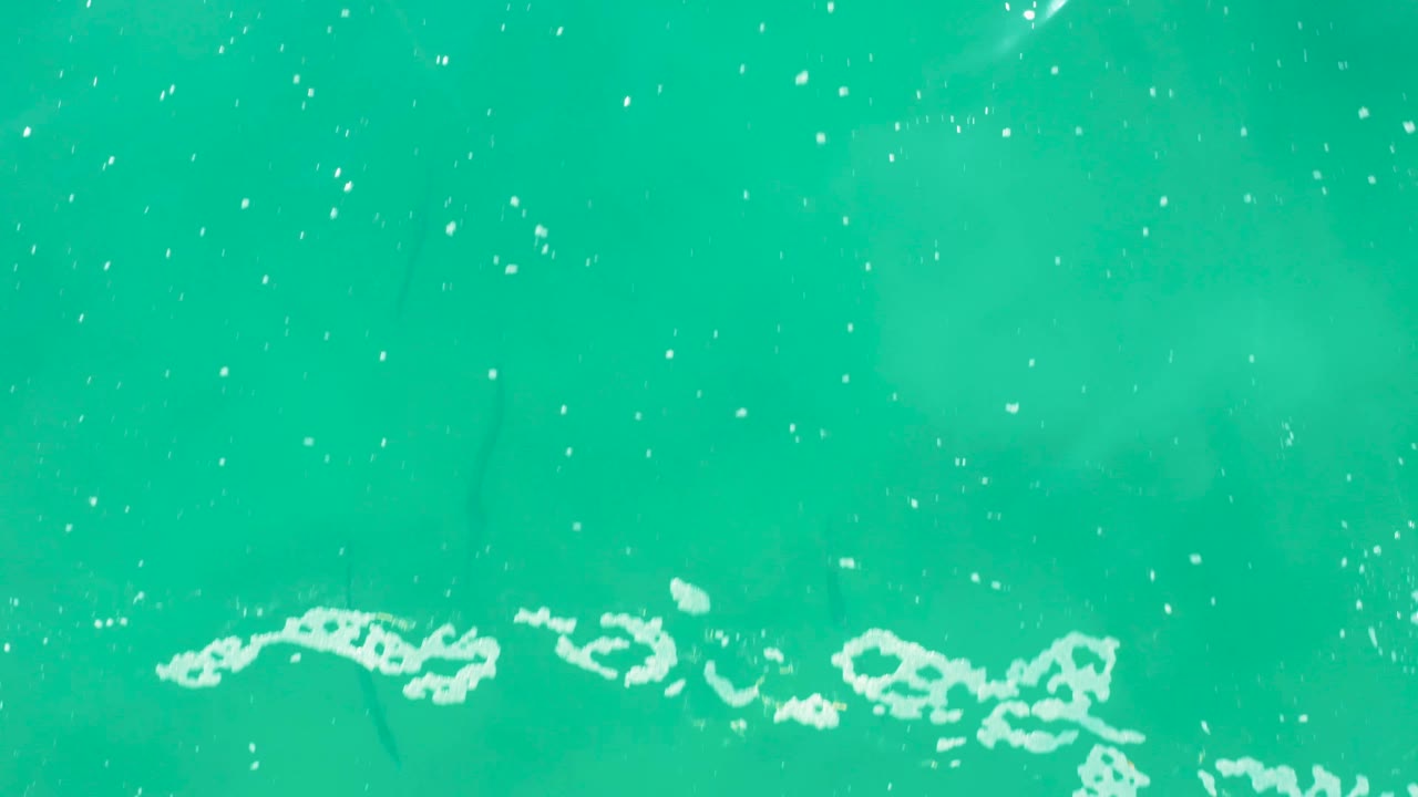 Overhead turquoise water in Laguna Beach Los Cabos with a band of white foam entering along the lower edge and fine bubbles scattered above it, with no visible people.