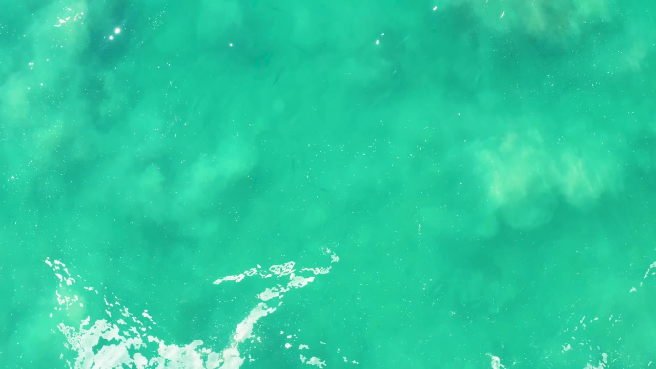 Overhead view of clear turquoise ocean water at Laguna Beach Los Cabos with white foam entering near the lower edge and no visible people.