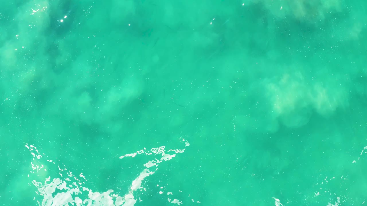 Clear blue-green ocean water at Laguna Beach Los Cabos shows a narrow white foam streak across the lower part of the overhead frame, with no visible people.
