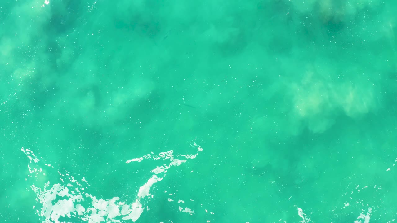 Turquoise sea surface at Laguna Beach Los Cabos with pale foam clustered near the lower center and soft underwater texture visible, with no visible people.